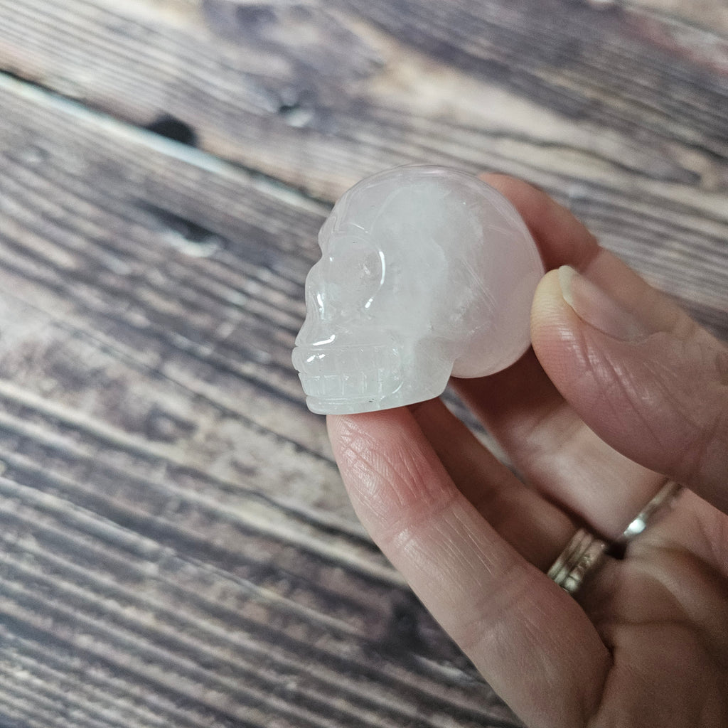 A carved pink crystal skull held in a hand