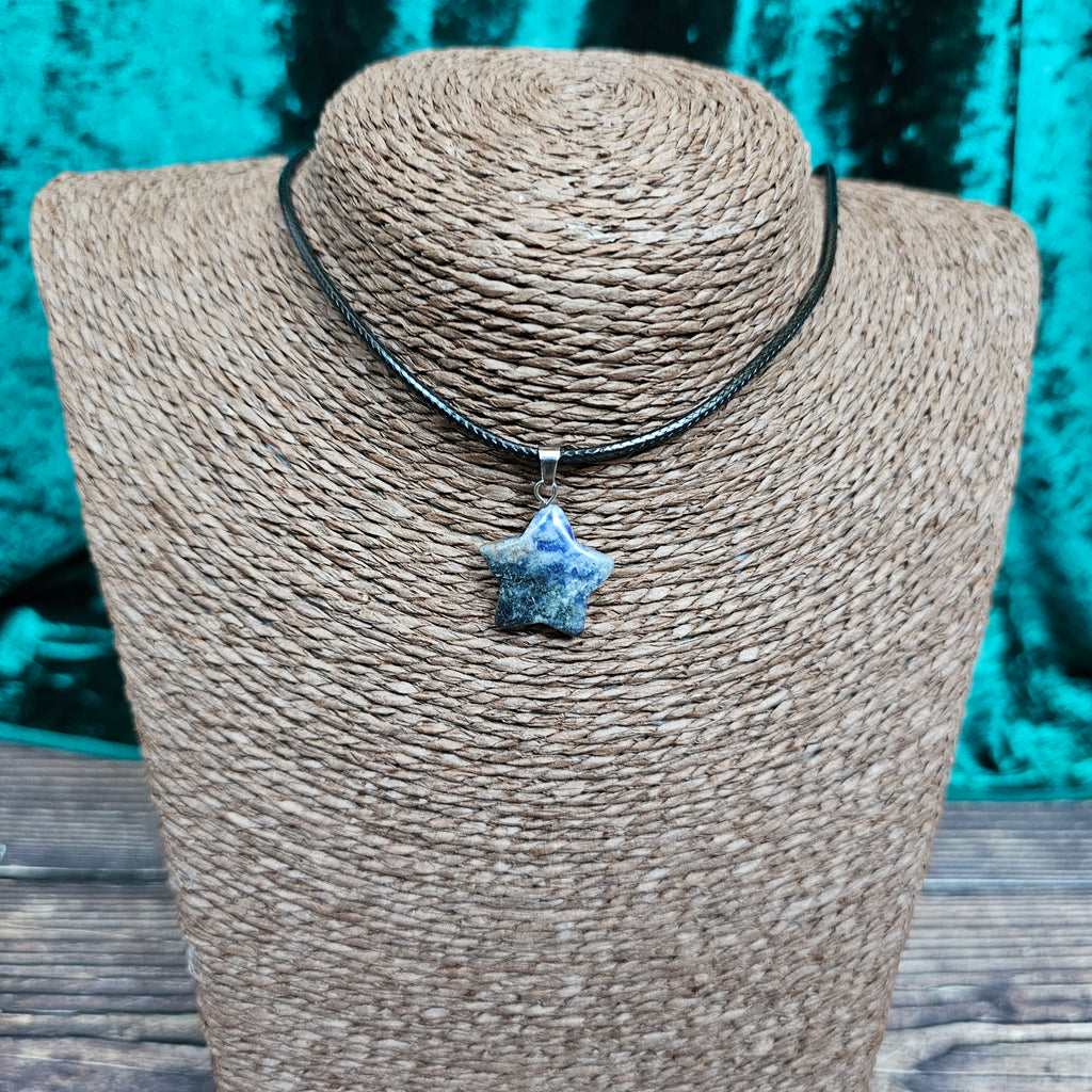 A star-shaped crystal pendant displayed on a brown mannequin, with a black cord.