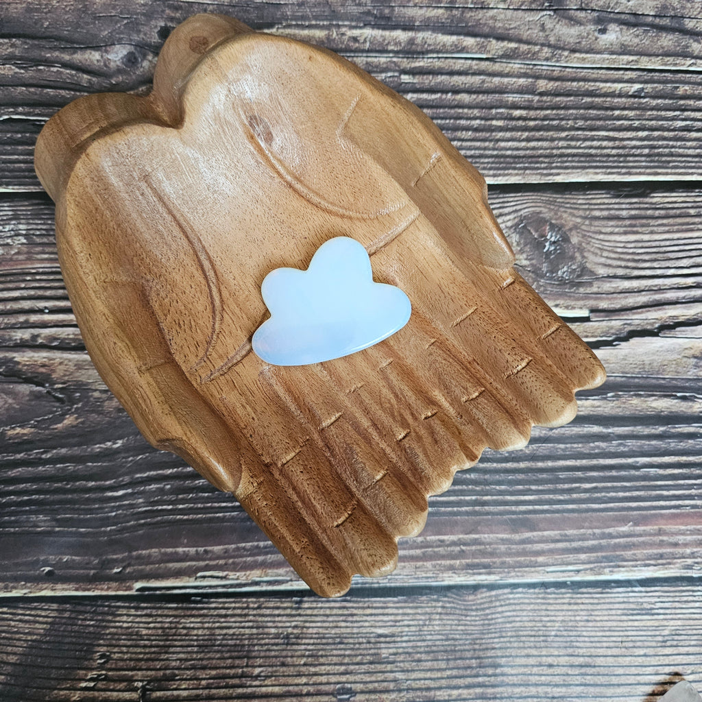 Carved Opalite crystal shaped like clouds, placed on a wooden surface.