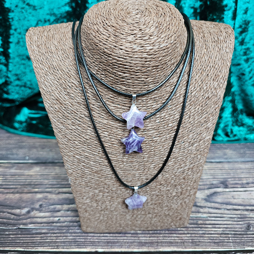 Three star-shaped crystal pendants in displayed on a brown mannequin, with a black cord.