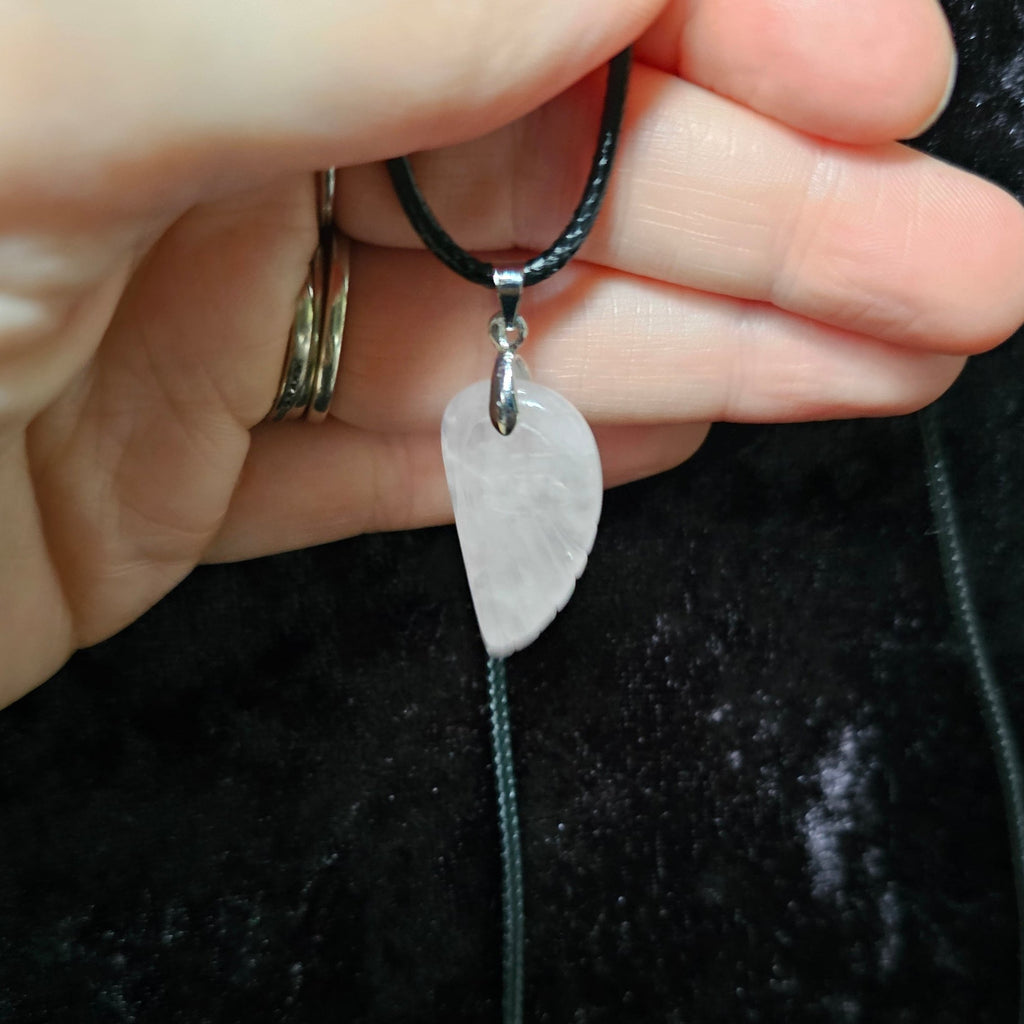 An angel wing-shaped crystal pendant attached to a black cord necklace, held in a person's hand.