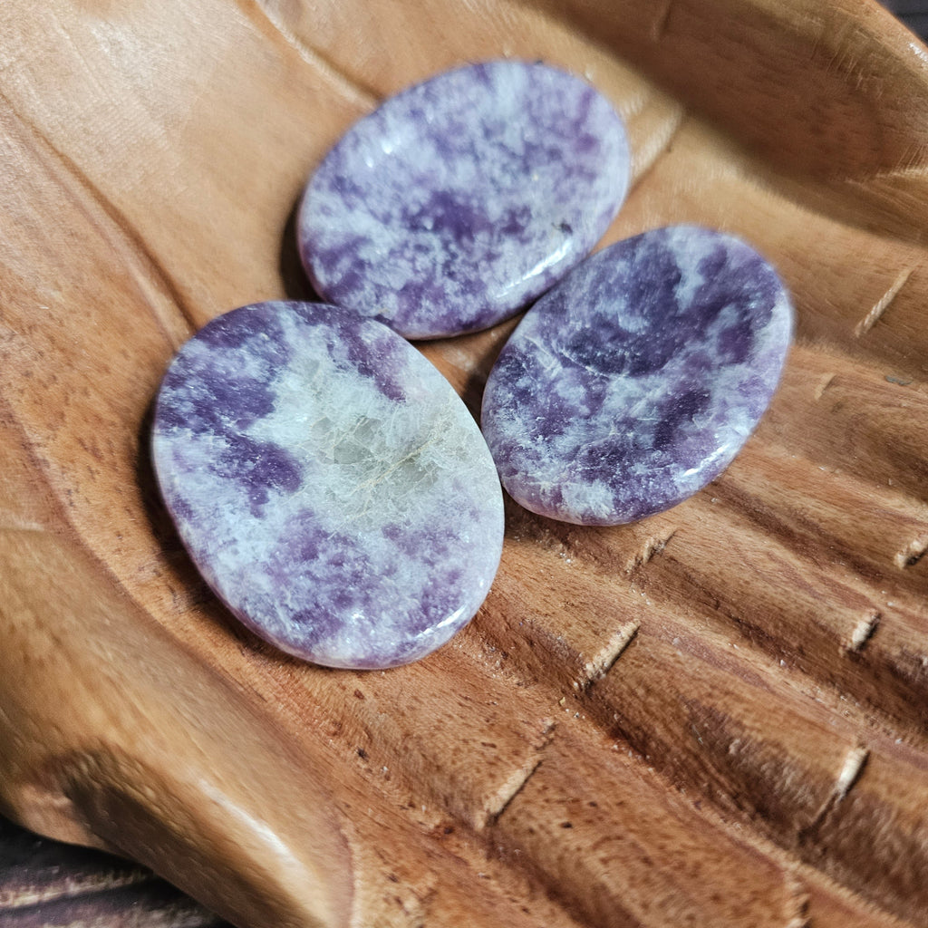 Three light purple polished crystal thumbstones resting on a wooden surface