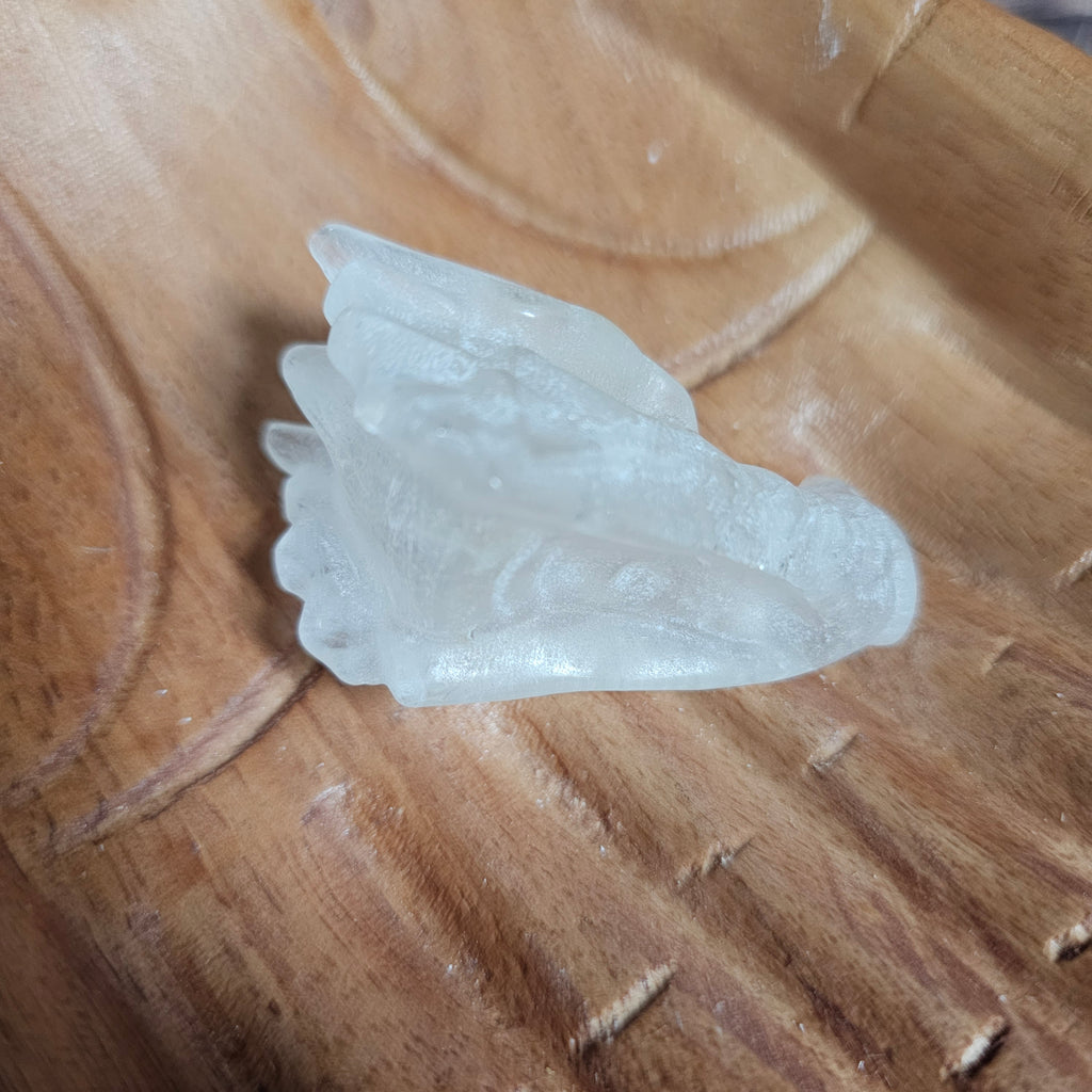 A clear quartz crystal dragon skull figurine, placed on a wooden surface.