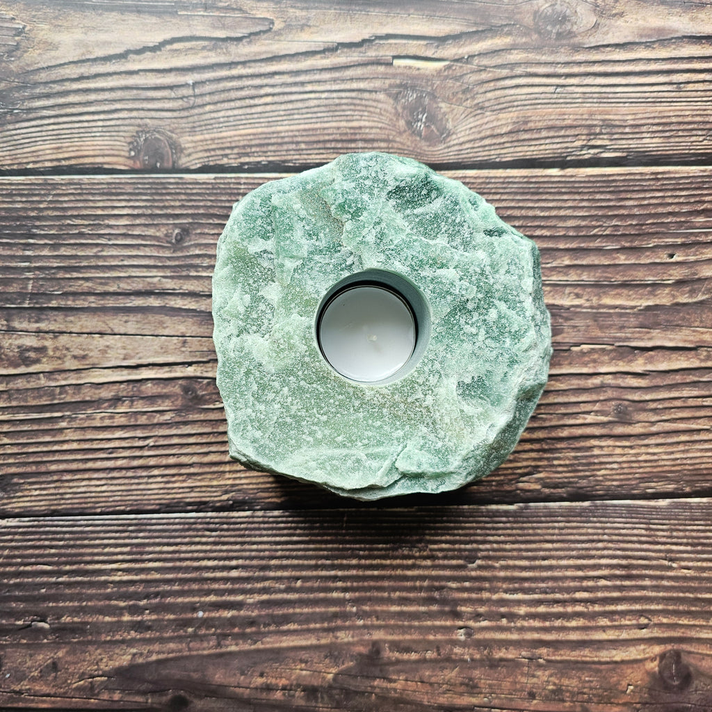 A chunky rough, green aventurine stone tealight holder placed on a wooden surface.