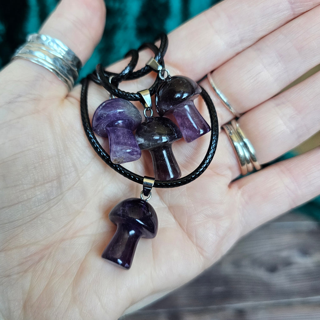 A collection of purple mushroom-shaped crystal pendants attached to black cords, held in a person's hand.