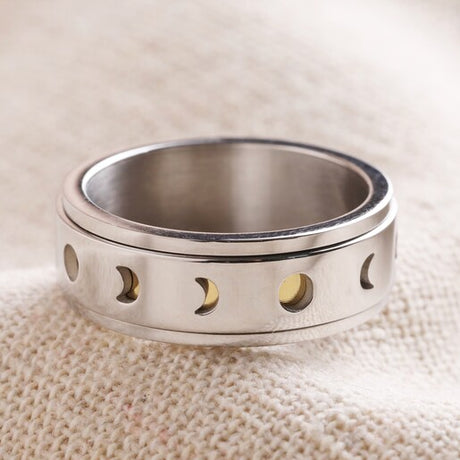 A polished silver ring with moon phase cut-outs and gold details on a textured background.