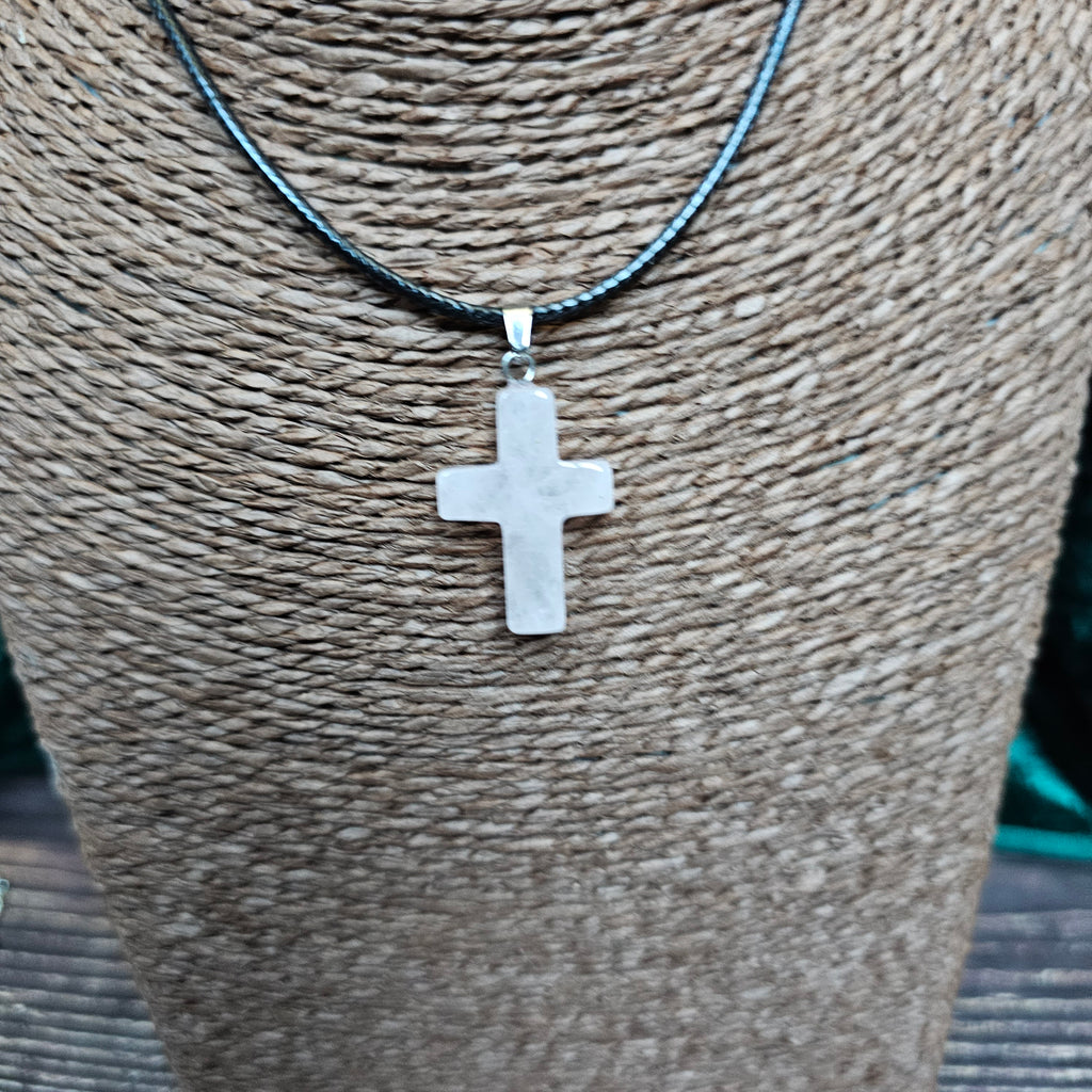 A cross-shaped crystal pendant with a black cord necklace displayed on a textured background.