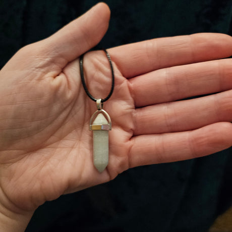 A hand holding a crystal pendant necklace with black cord
