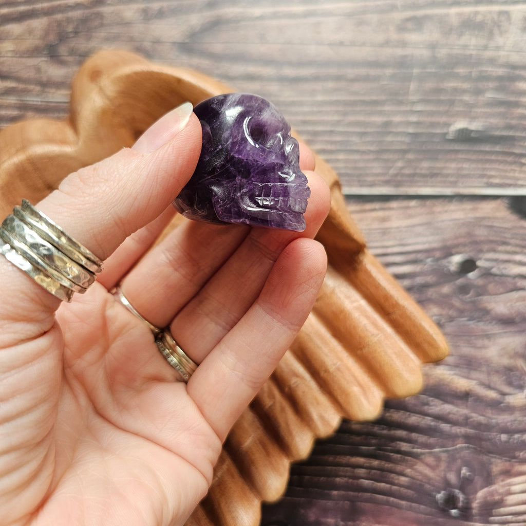 A carved Amethyst crystal skull held in a hand to the side