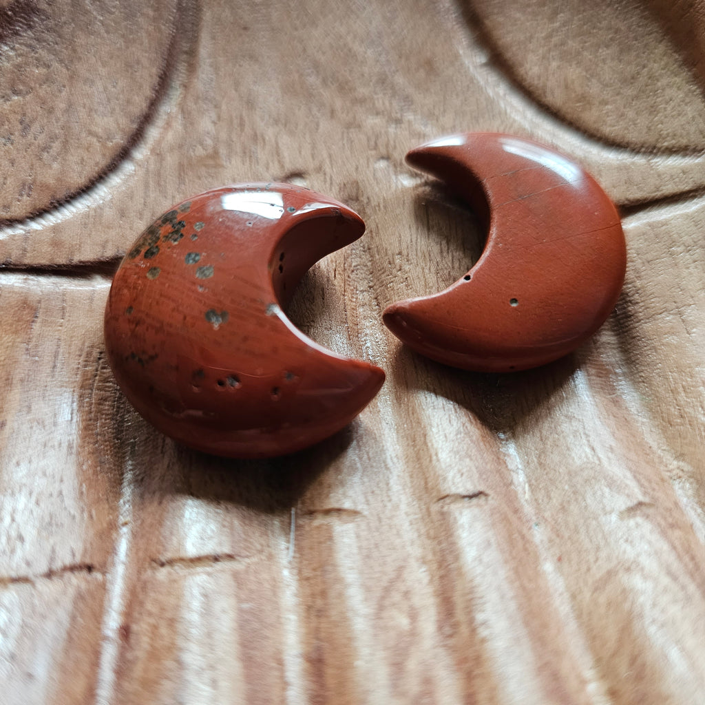Two red jasper crescent moon shaped crystals placed on a pair of wooden hands 
