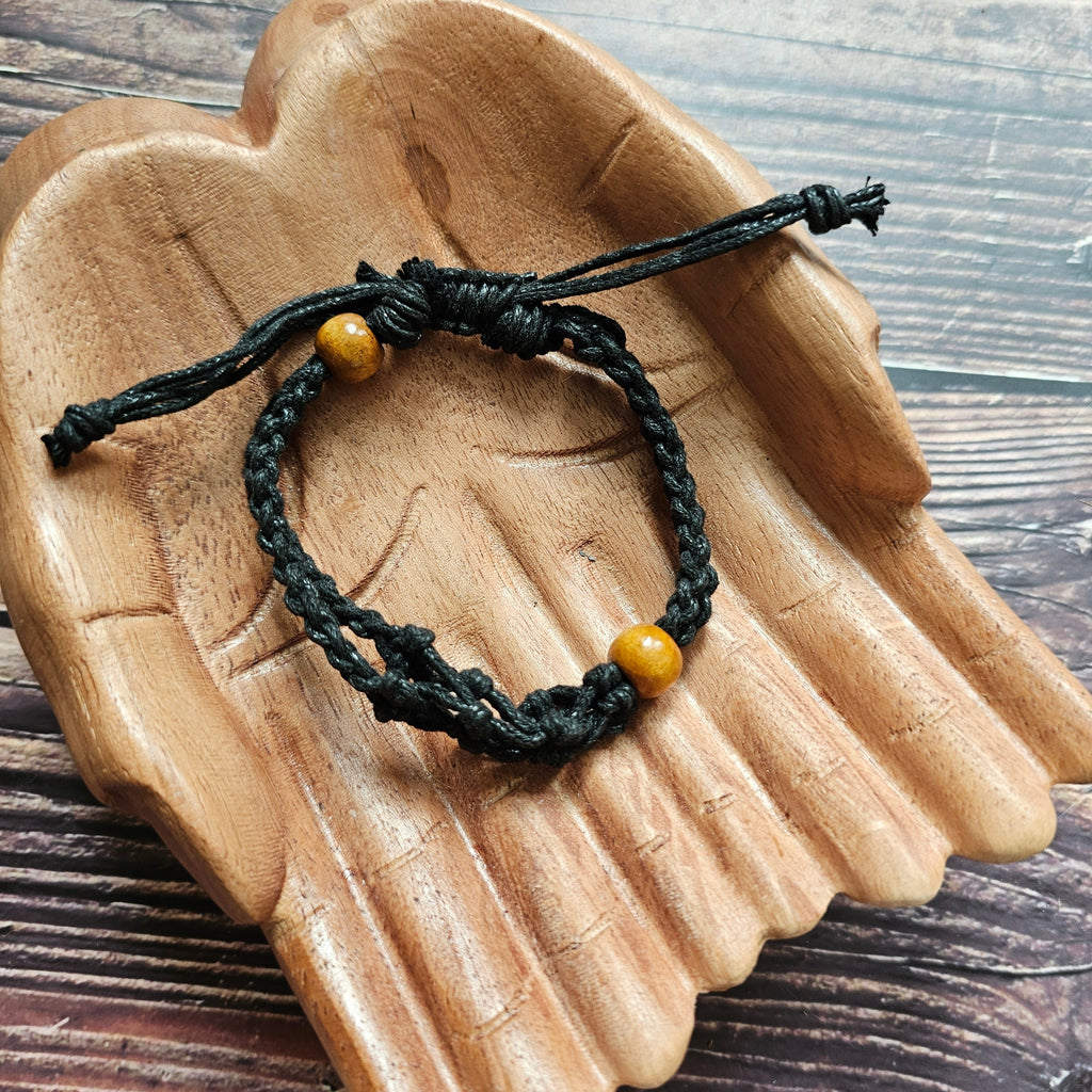 A black-coloured crystal cord bracelet laid on a pair of wooden hands 