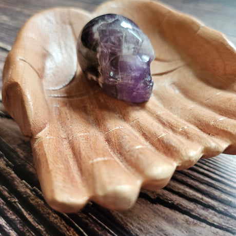 A carved Amethyst crystal skull placed on a wooden, hand-shaped dish