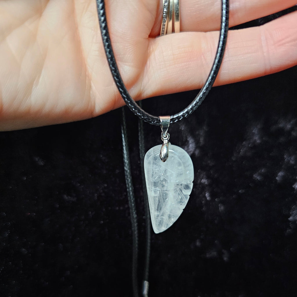 An angel wing-shaped crystal pendant attached to a black cord necklace, held in a person's hand.