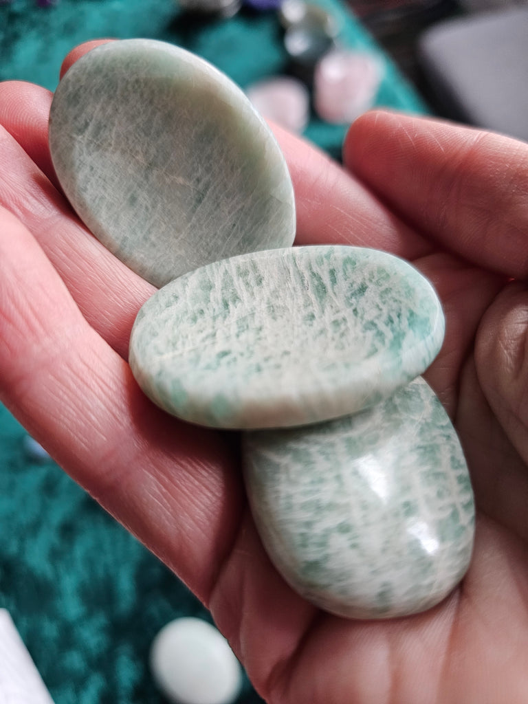 Three greeny blue polished crystal thumbstones being held in a hand