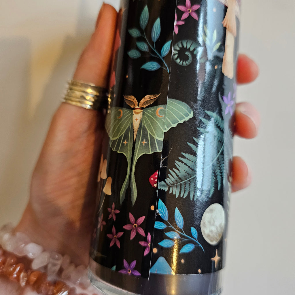 A close up of a tube candle with a label 'Wildberry Scented Candle' and an illustration of mushrooms and leaves. It is being held in a hand and showing that the design does not quite line up. 