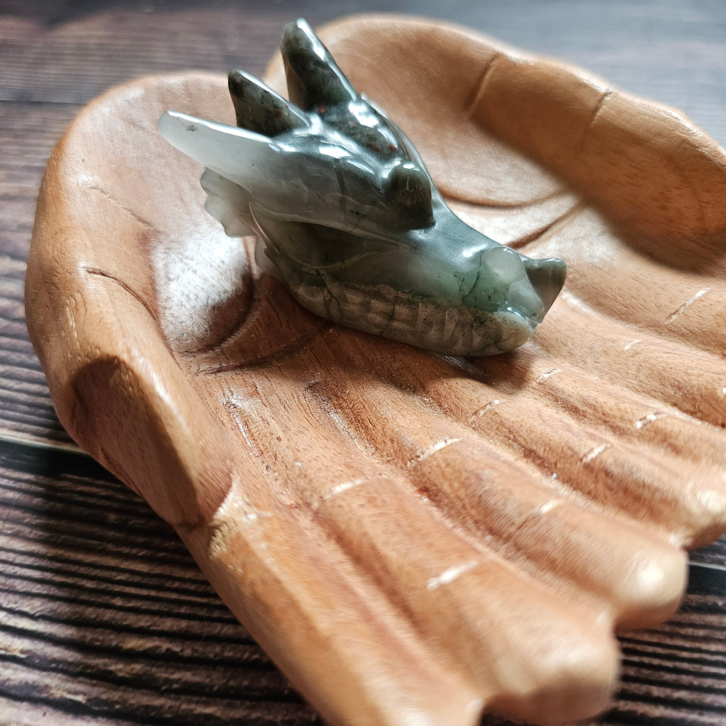 A green crystal dragon skull figurine, placed on a wooden surface.