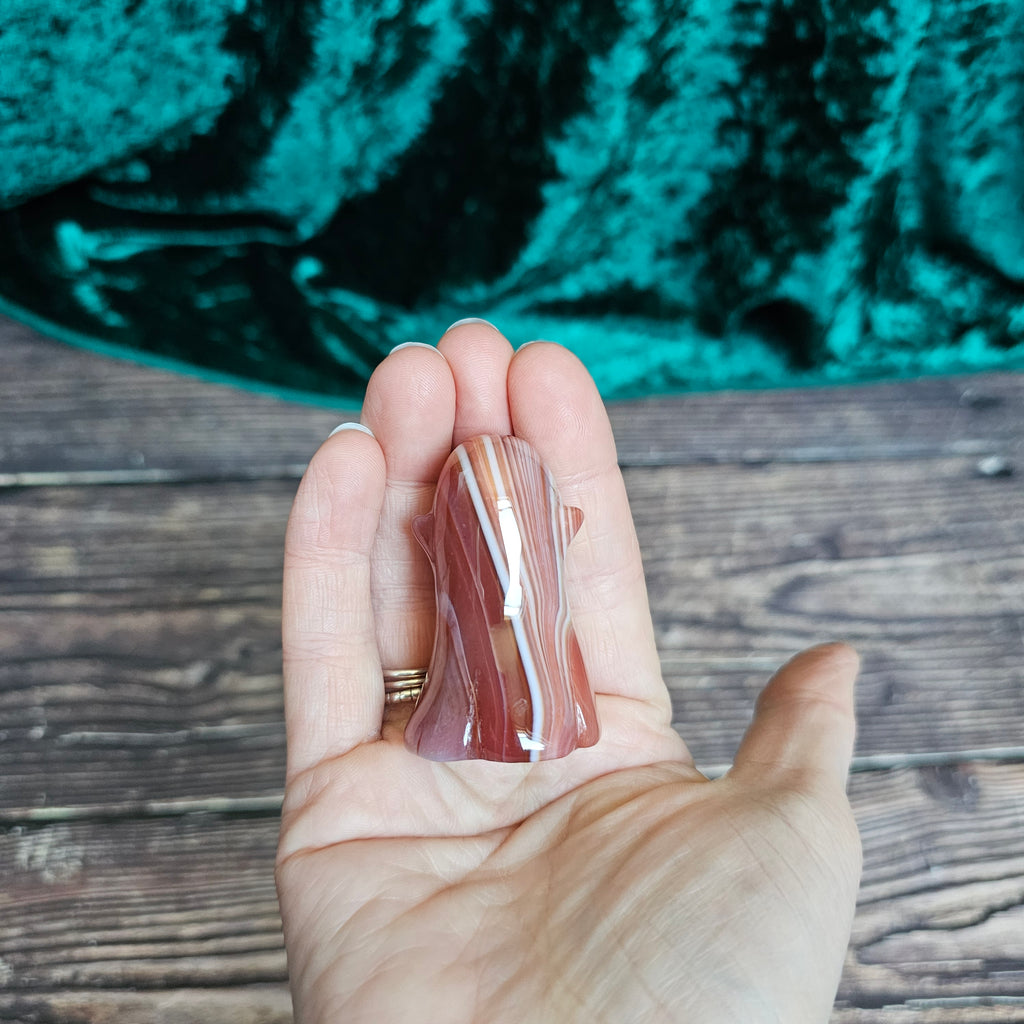 The back of a Carnelian carved crystal ghost held in a person's hand