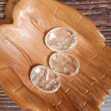 Three clear quartz polished crystal thumbstones resting on a wooden surface