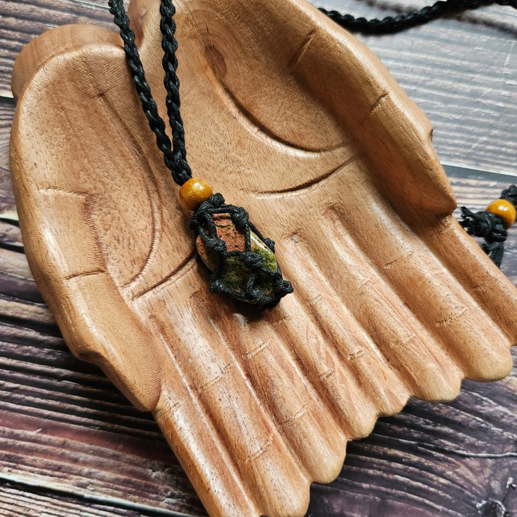 A black-coloured crystal cord necklace with an example crystal inside laid on wooden hands