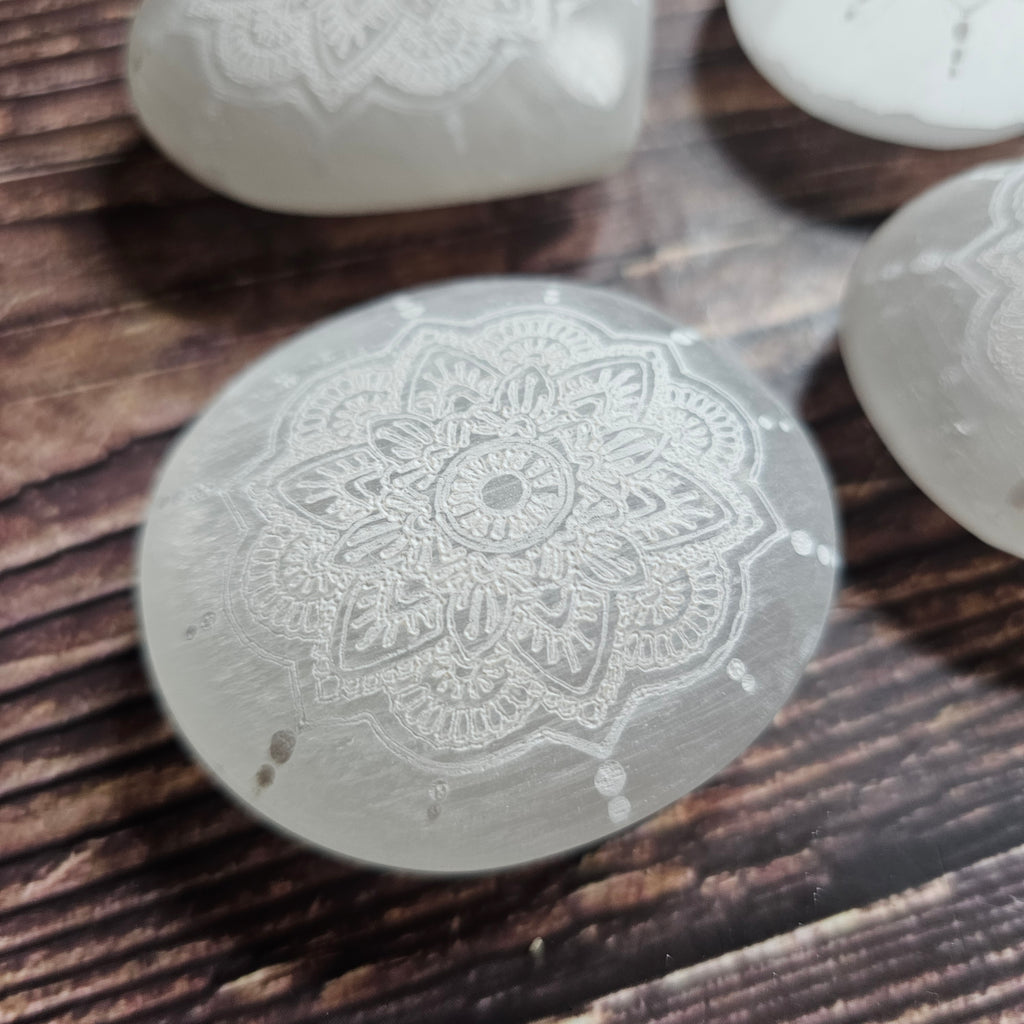 A Selenite oval, carved with intricate mandala design, laid on a wooden surface
