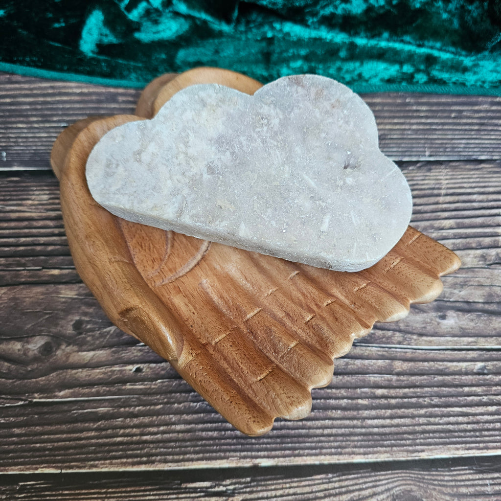 A carved Pink Amethyst crystal shaped as a cloud laid on a pair of wooden hands