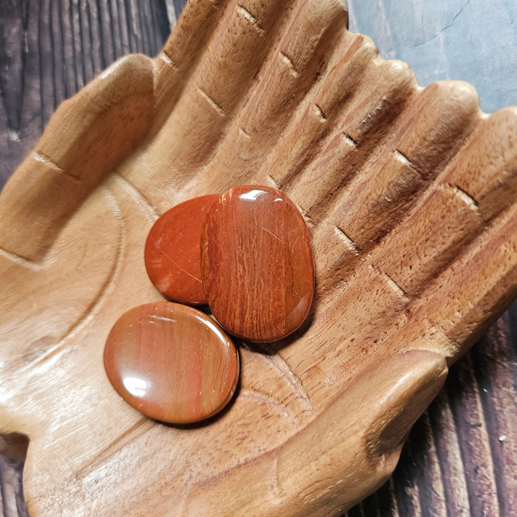 Three red polished crystal thumbstones resting on a wooden surface