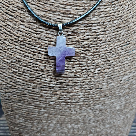 A cross-shaped crystal pendant with a black cord necklace displayed on a textured background.