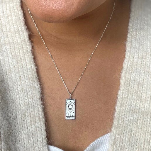 A close up of someone wearing a silver tarot necklace with a pendant featuring a rectangular design, the 'Sun' card from tarot.
