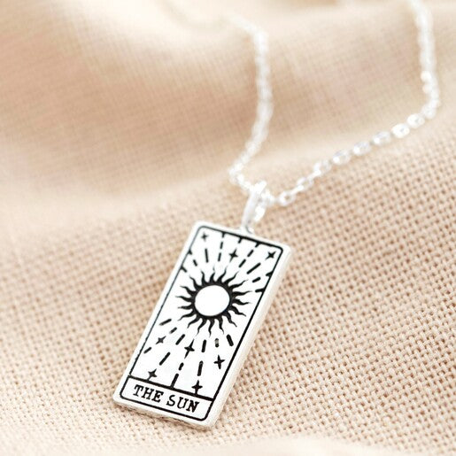 A close up of a silver tarot necklace with a pendant featuring a rectangular design, the 'Sun' card from tarot.