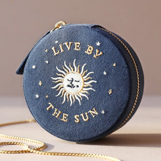 A closed navy blue travel jewellery case with gold embroidery, featuring an embroidered "live by the sun" design and a zippered top